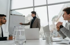 Professionals engaged in a collaborative business meeting with charts and laptops in a modern office setting. — "Behind the C